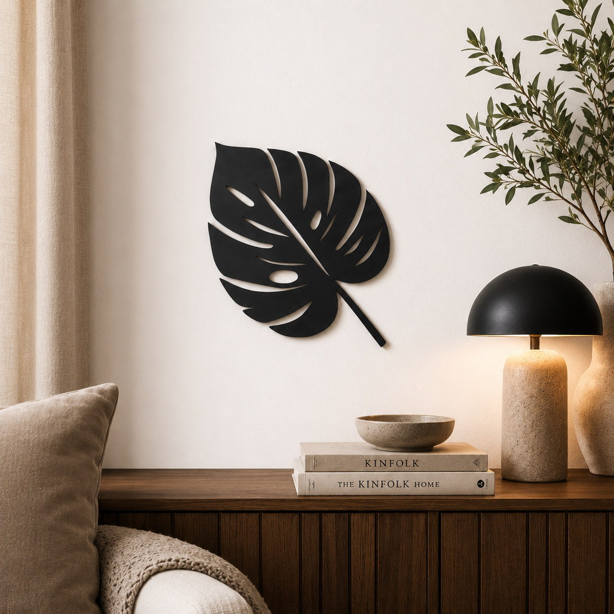 Monstera Schild an der Wand über dunklem Sideboard, dekoriert mit Lampe und Kissen